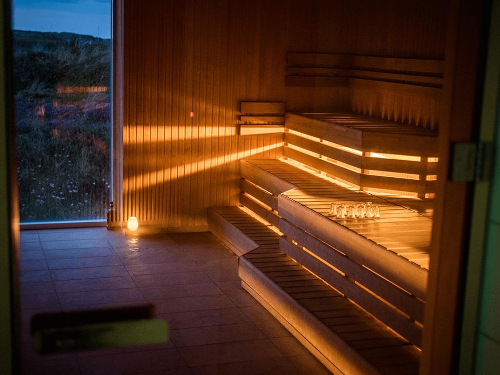 En moderne sauna med blødt lys og træbænke, der skaber en afslappende atmosfære.