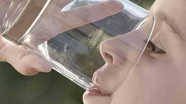 Barn drikker vand fra et glas, mens det holder glasset tæt på ansigtet.