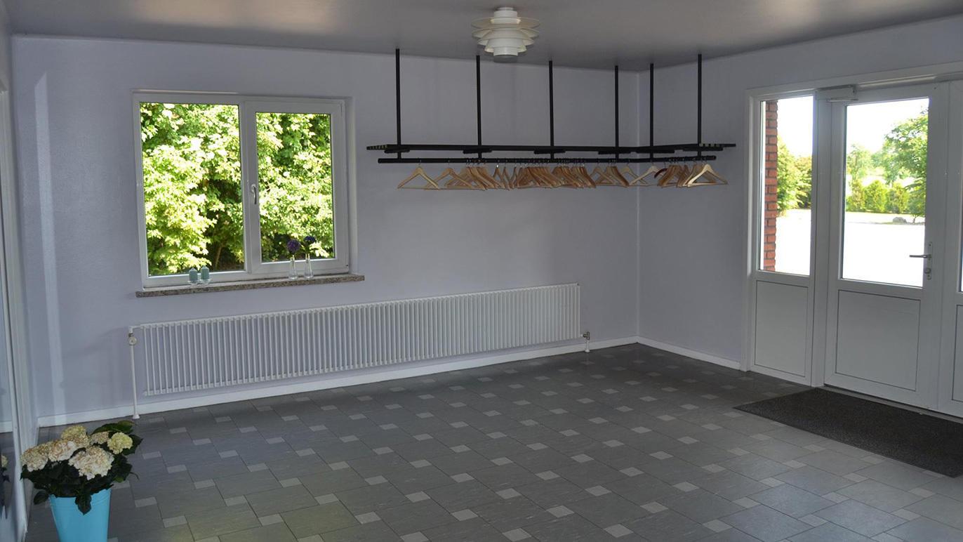 Lyst rum med vinduer, radiator, og en garderobe med knager, samt en dør til udendørsområdet.