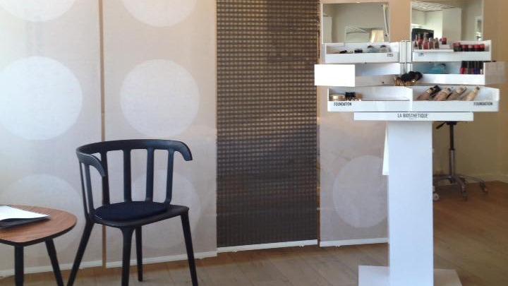 En frisørsalon med en sort stol, et rundt bord og en makeup-display med forskellige skønhedsprodukter.