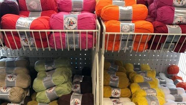 Farverigt garn i forskellige nuancer stablet på hylder i en garnbutik.
