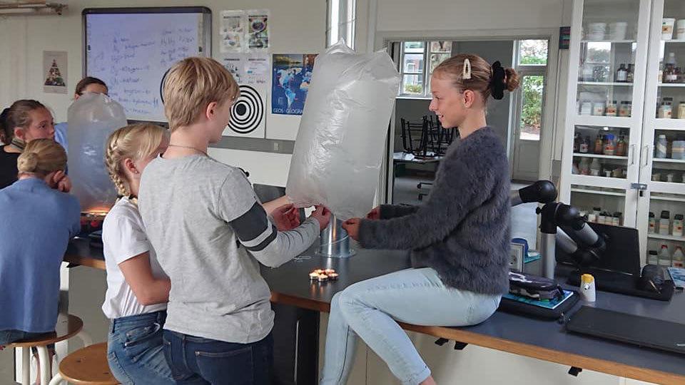Elever udfører et eksperiment i et klasseværelse med en stor ballon og laboratorieudstyr.