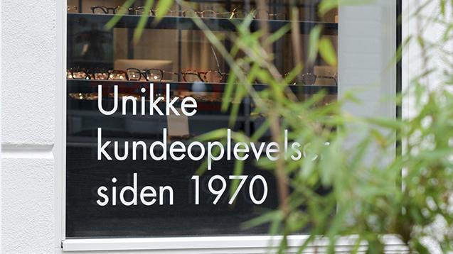 Unik butiksvindue med teksten "Unikke kundeoplevelser siden 1970" og grønne planter i forgrunden.