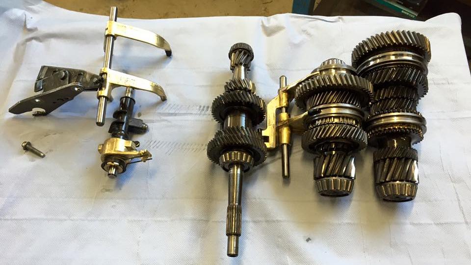Billede af gearkomponenter og værktøj til reparation af motor, placeret på en hvid overflade.