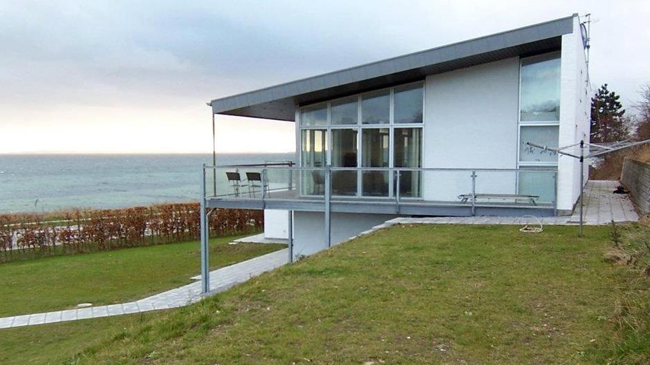 Moderne hus ved kysten med store vinduer og græsplæne, der vender ud mod havet.