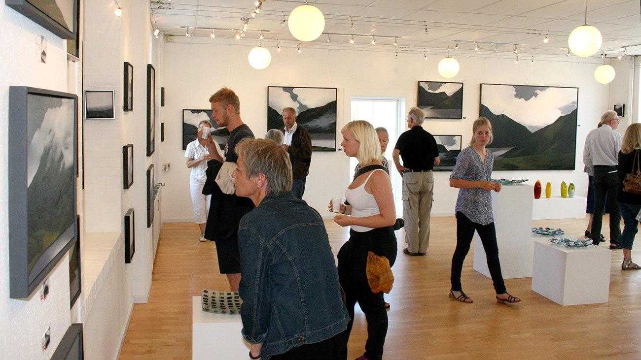 Besøgende i et kunstgalleri ser på malerier og skulpturer under en udstilling med moderne kunst.