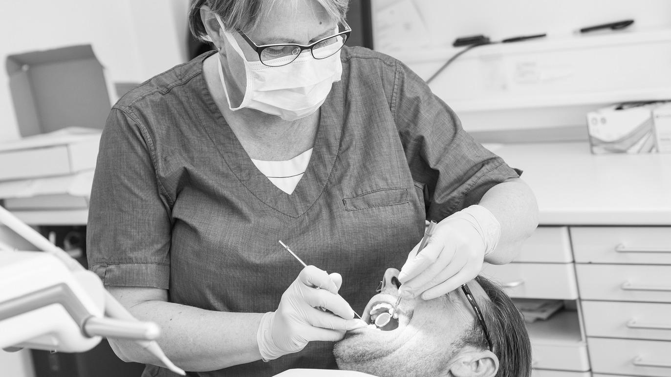 En tandlæge undersøger en patients tænder i en klinik, iført maske og handsker.