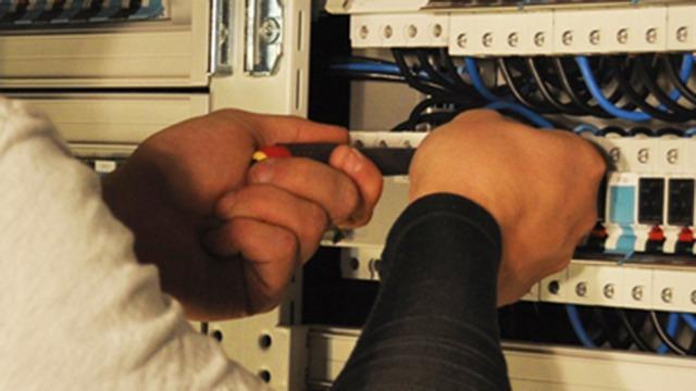 Håndværker arbejder med værktøj på elektriske installationer i et skab med ledninger.