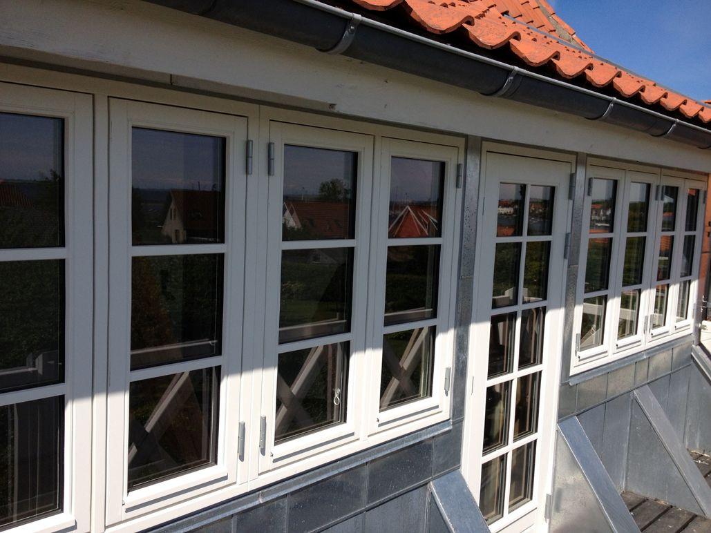 Flere vinduer på en bygning med rød tagsten og grå facade, beliggende i et solrigt område.