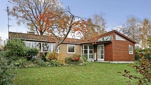 Et moderne hus med træfacade og store vinduer, omgivet af en velplejet have i efterårsfarver.