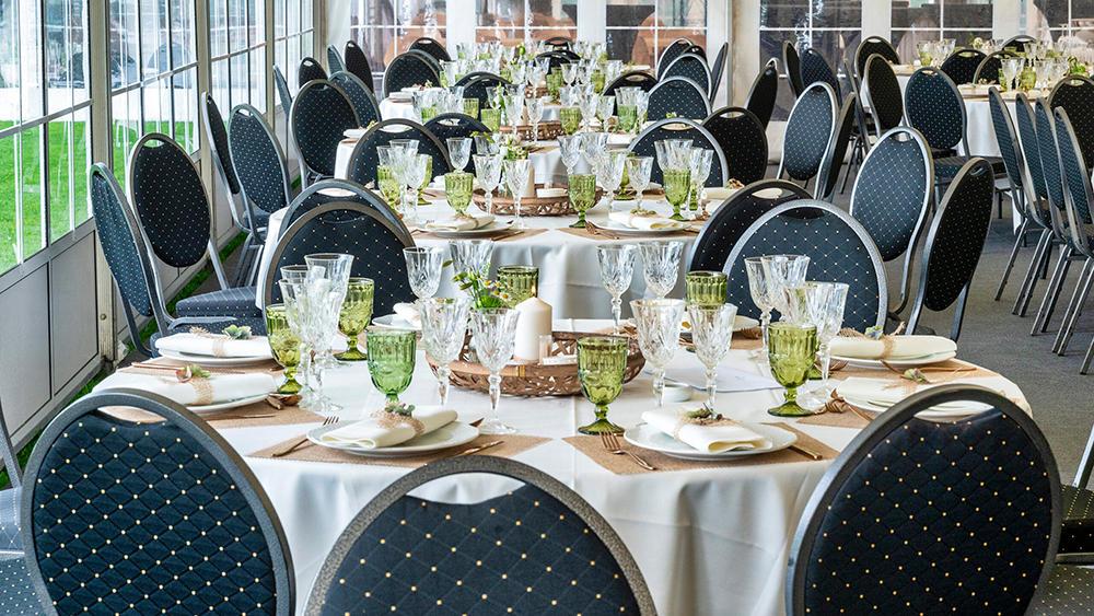 Elegant festlokale med dækkede borde, grønne glas og sorte stole i en lys atmosfære.