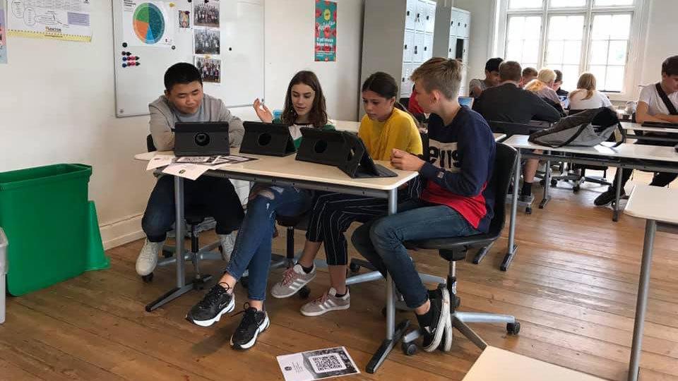 Fire elever sidder ved borde i et klasseværelse og arbejder på tablets.