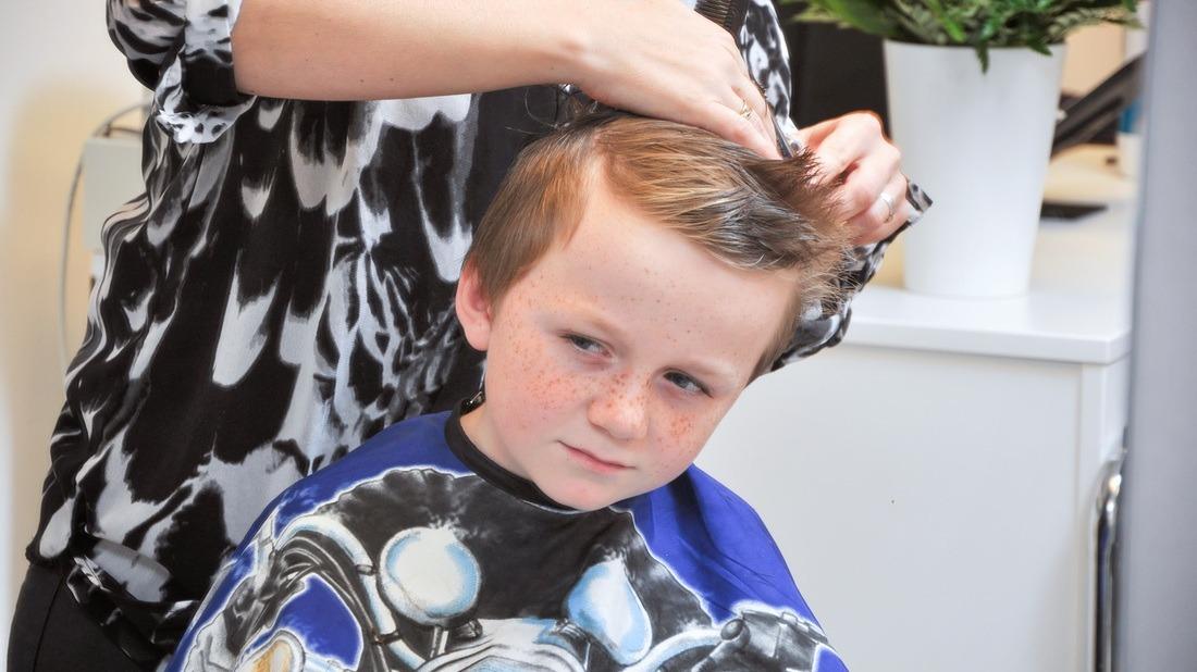 En dreng får en frisure i en frisørsalon, mens en frisør styler hans hår.
