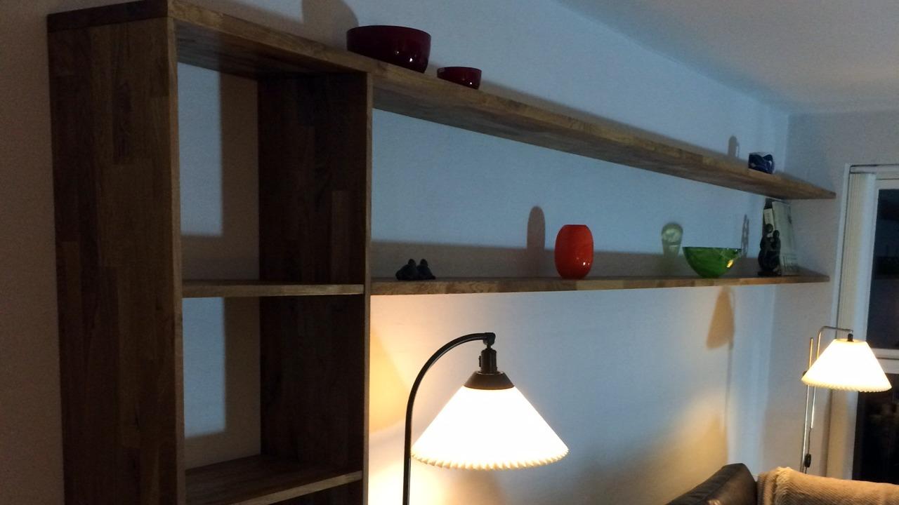 Reol med åbne hylder i træ, dekoreret med farverige genstande og to lamper i stuen.