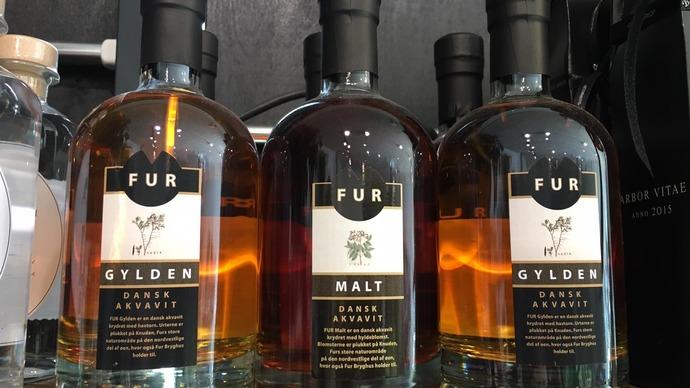 Flasker med Fur gylden og malt spiritus på en hylde, hver med et elegant etiketdesign.
