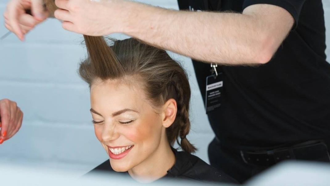 En frisør styler hår på en glad kvinde i en salon, mens hun smiler og ser tilfreds ud.