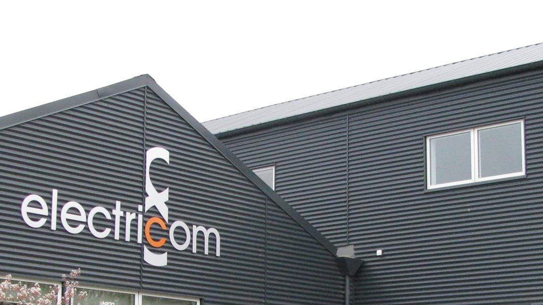 Bygning med sort facade og logoet "electriCom" på væggen. Vinduet er synligt på den øverste etage.