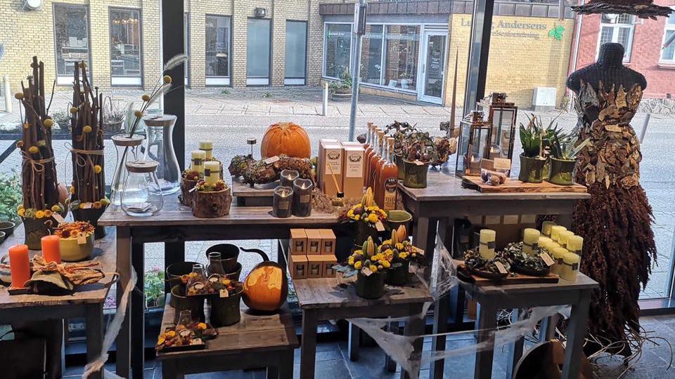 En smuk udstilling med efterårsdekorationer, lys, græskar og planter i en butik.