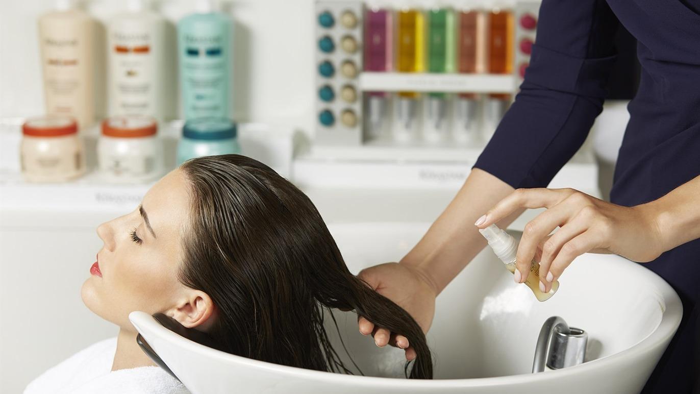 En kvinde får hårvask i en frisørsalon, mens en frisør anvender shampoo ved en vaskestation.