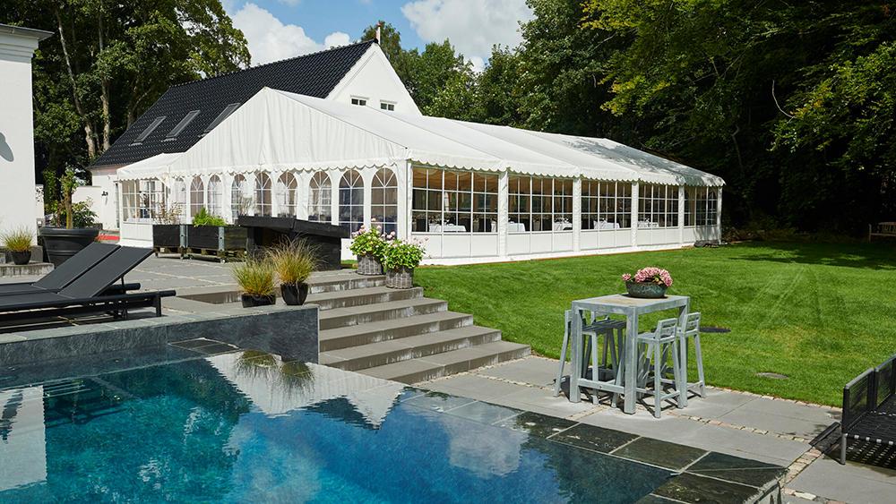 Et stort hvidt telt ved en moderne villa med swimmingpool og grøn græsplæne.