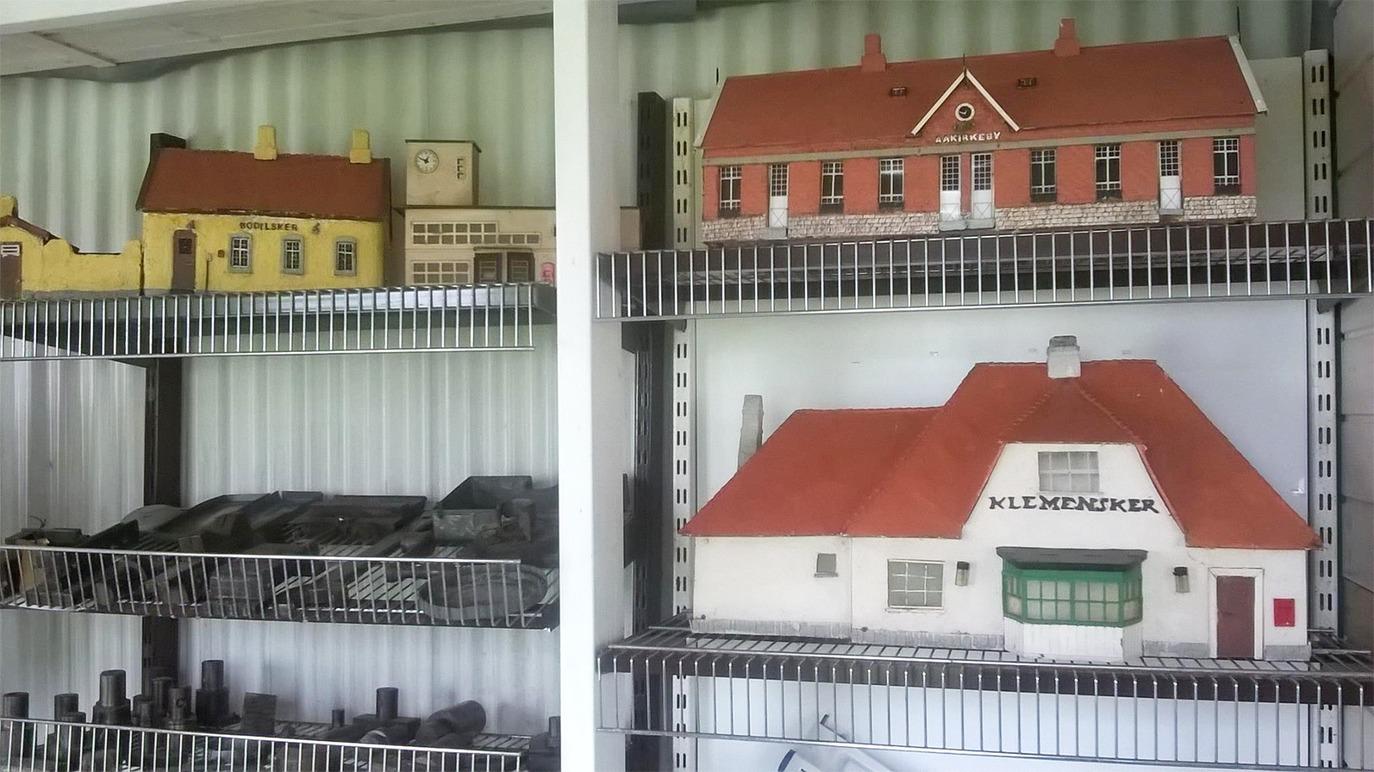 Modelbygninger og tog i en hylde, herunder en rødtagget bygning og en station.