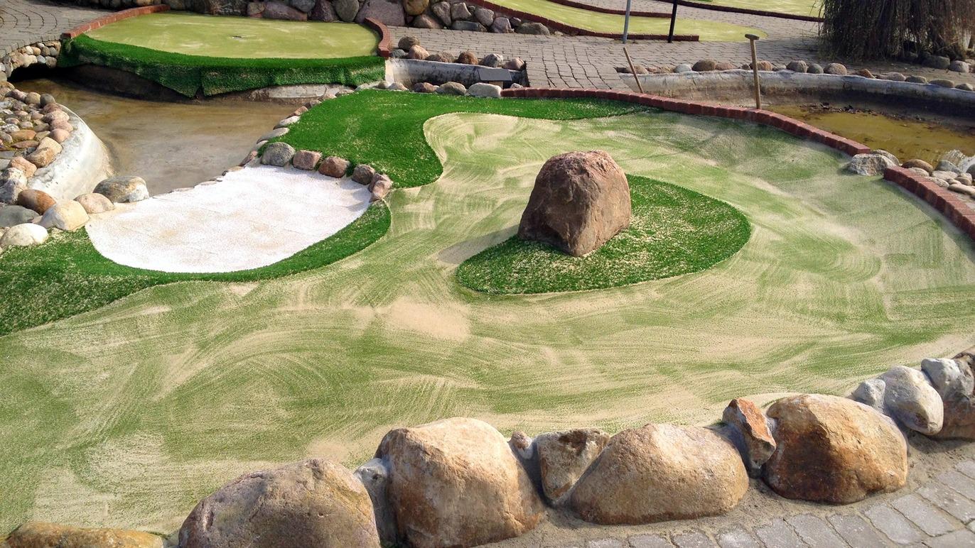 Minigolfbane med kunstgræs, sandbunker og store sten langs kanten.