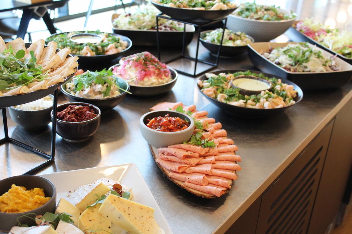 Frokostbuffet med forskellige salater, rejer, dips og ost på et bord i en lys restaurant.
