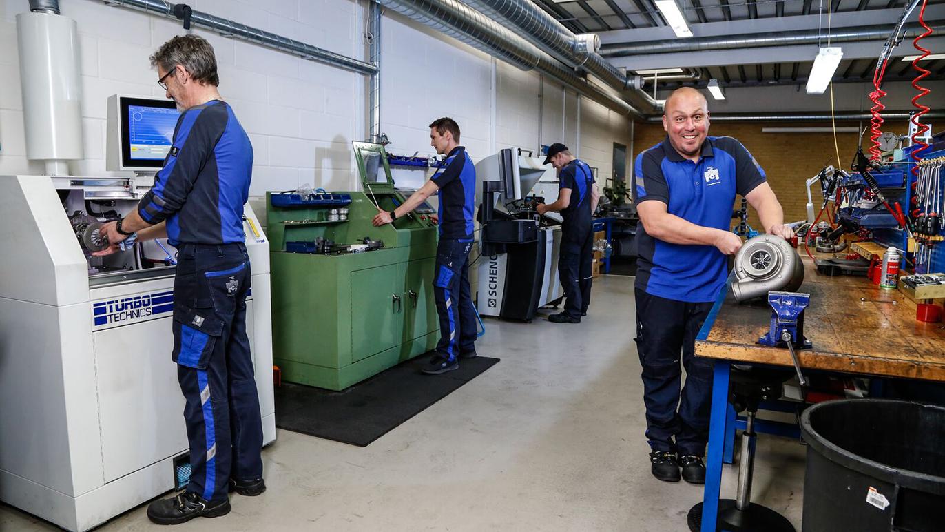 Mænd i blå arbejdstøj arbejder i en moderne værksted med maskiner og værktøj.