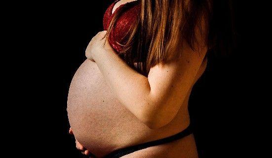 Gravid kvinde i rød bh, der holder sin mave, med fokus på hendes silhuet mod en sort baggrund.