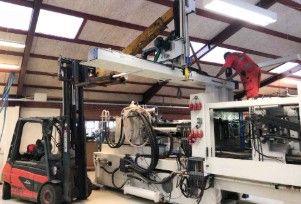 Industrielt produktionsmiljø med en gaffeltruck og en stor maskine med robotarme.