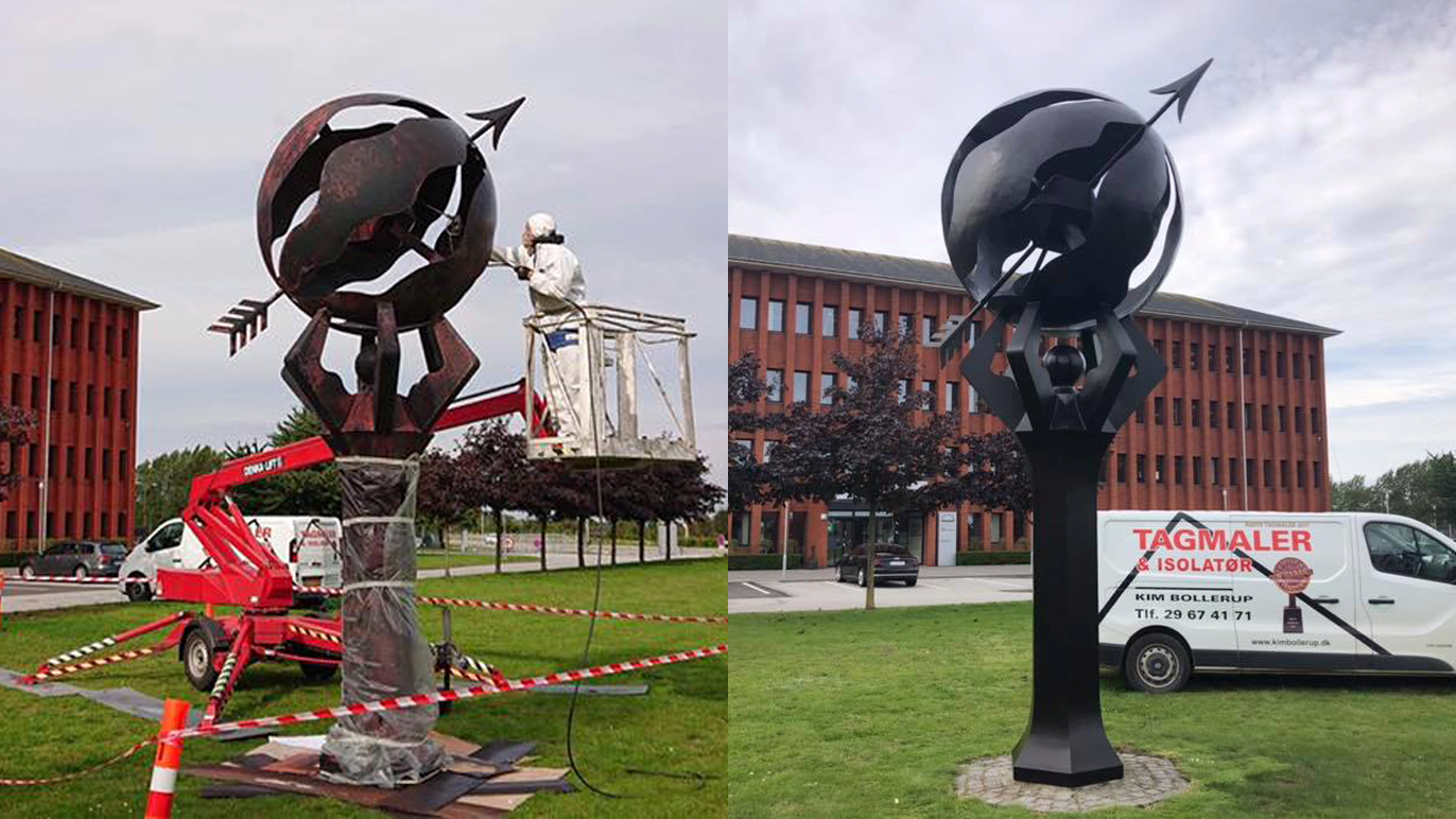 Skulptur af en globus med pile, der står på en sokkel, med en maler, der arbejder på den.
