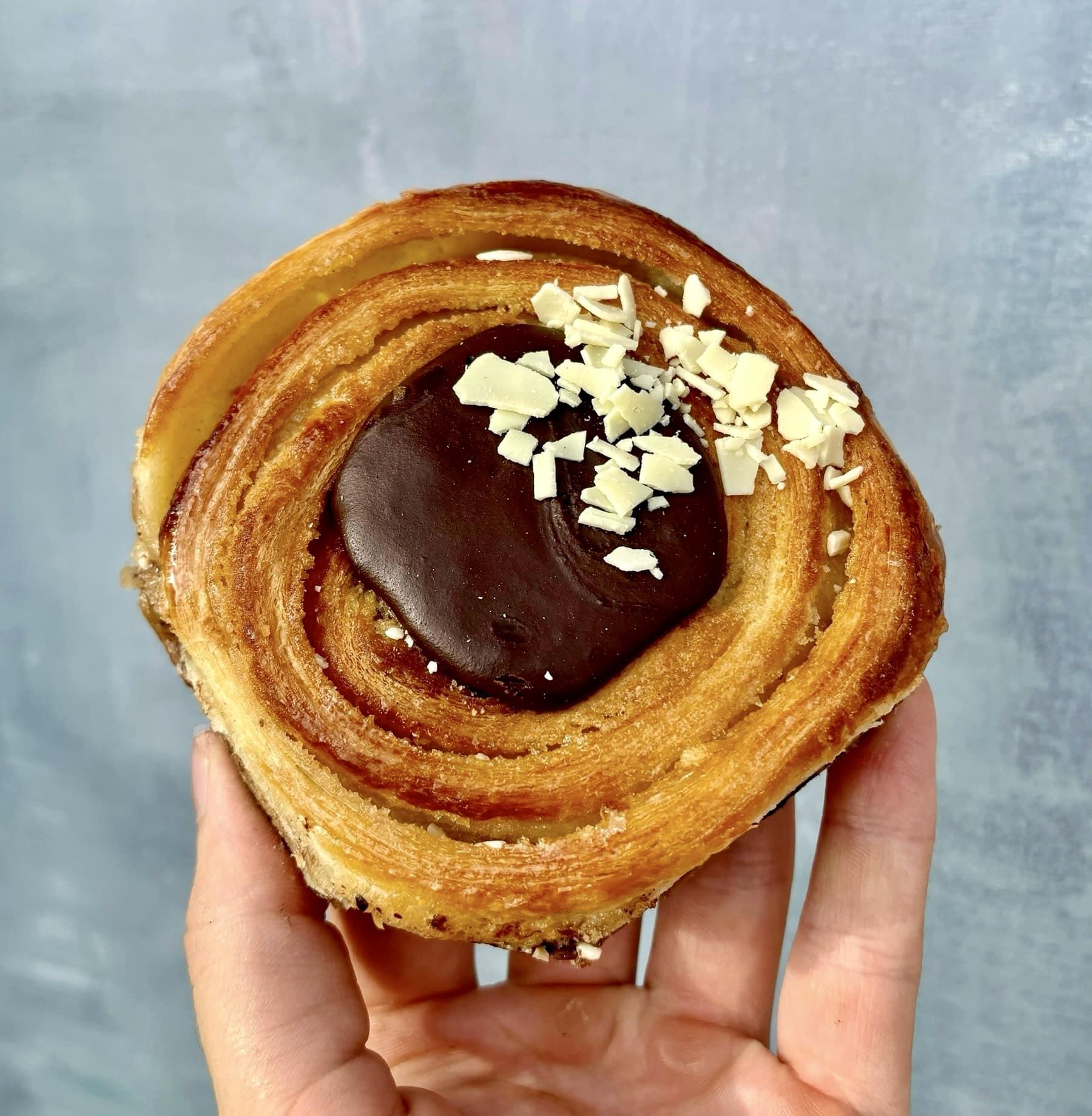 En hånd holder en lækker kanelbolle med chokoladefyld og hakket mandel på toppen.