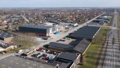 Luftfoto af en by med bygninger, veje og parkerede biler i et industriområde.