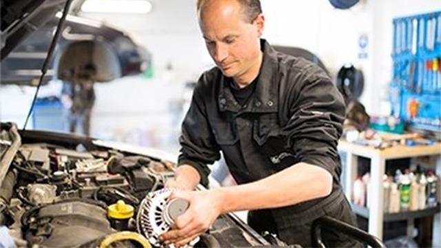 En mekaniker arbejder på en bilmotor i et værksted, mens han installerer en generator.