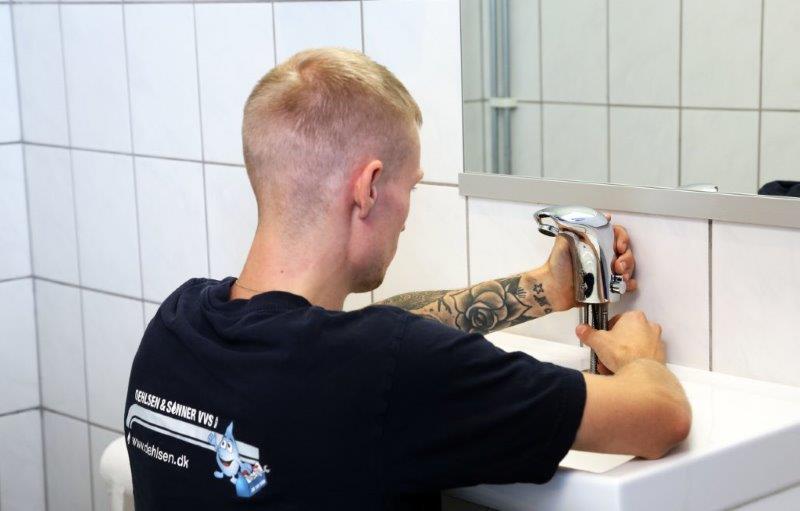 En ung mand installerer en vandhane i et badeværelse med fliser.