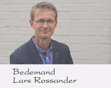 En smilende bedemand ved navn Lars Rossander står foran en lys væg iført en blazer.