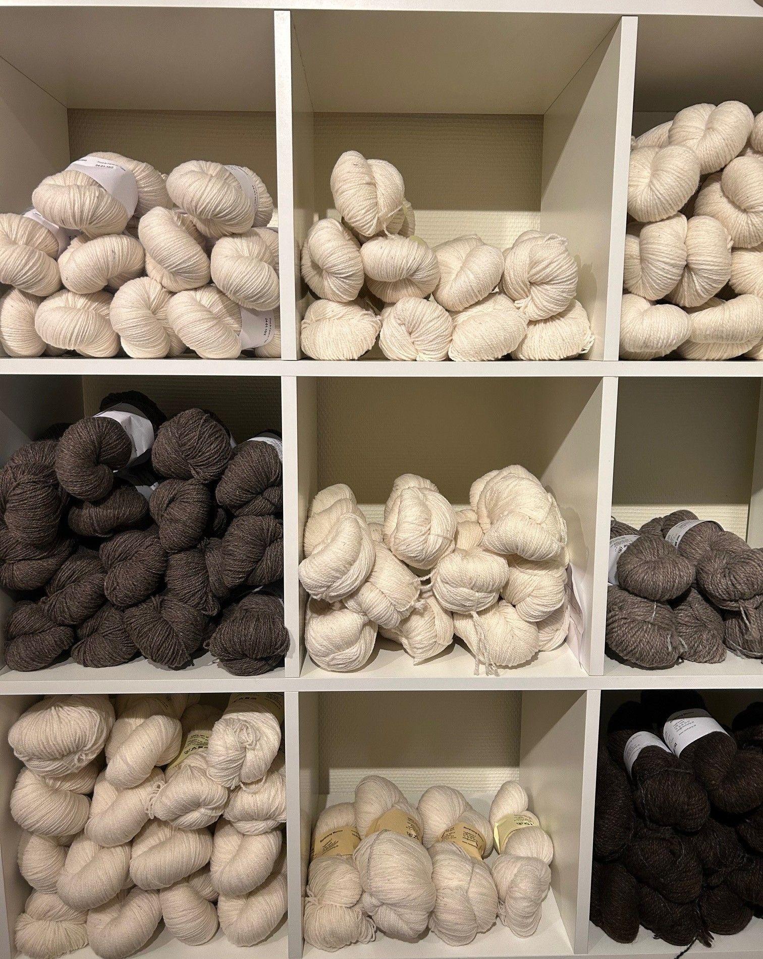 Hylder fyldt med garnnøgler i forskellige nuancer af beige og brun.