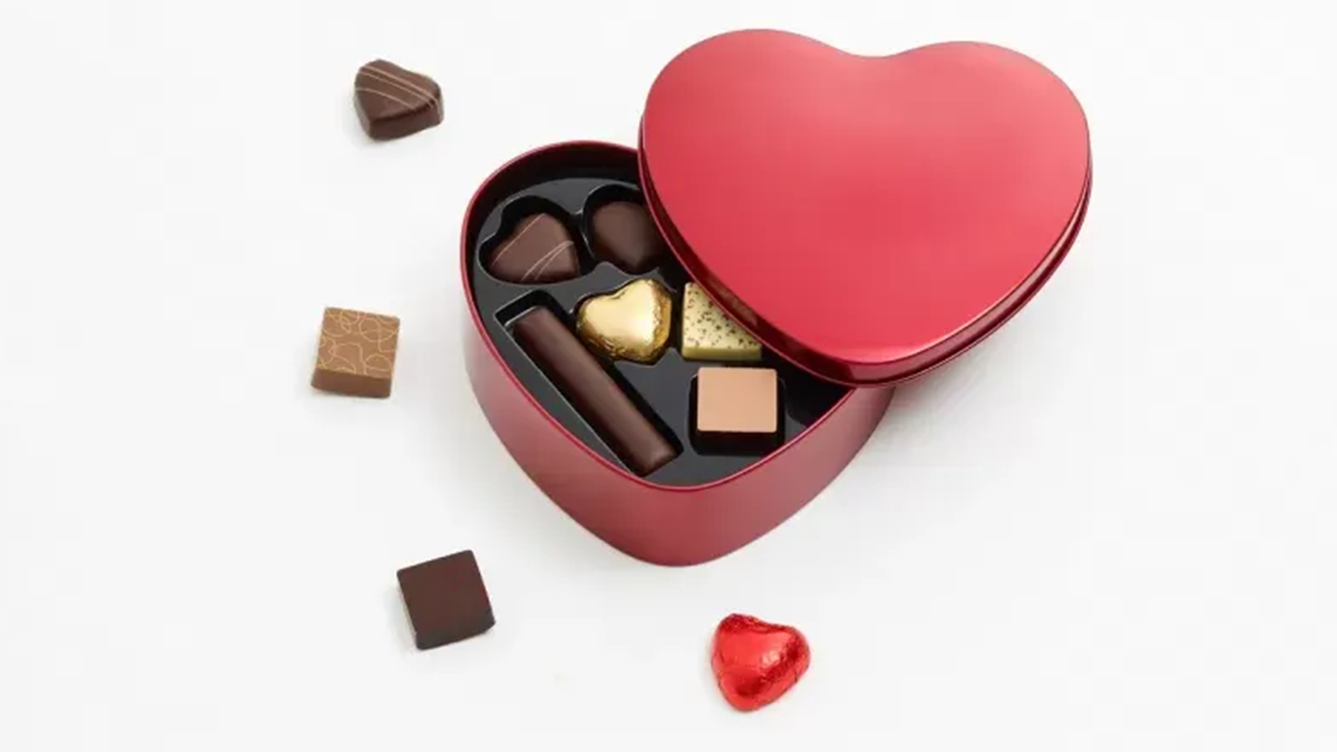 En rød hjerteformet æske med chokoladefyld og flere chokoladebidder omkring.