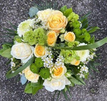 En smuk buket med gule og hvide roser, grønne blomster og friske blade på en grå overflade.