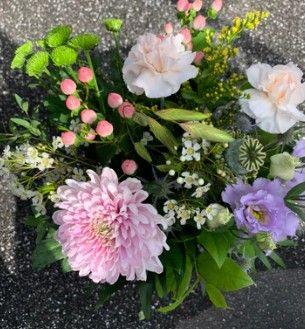 En farverig buket med lyserøde dahliaer, hvide nelliker, lilla blomster og grønne blade.
