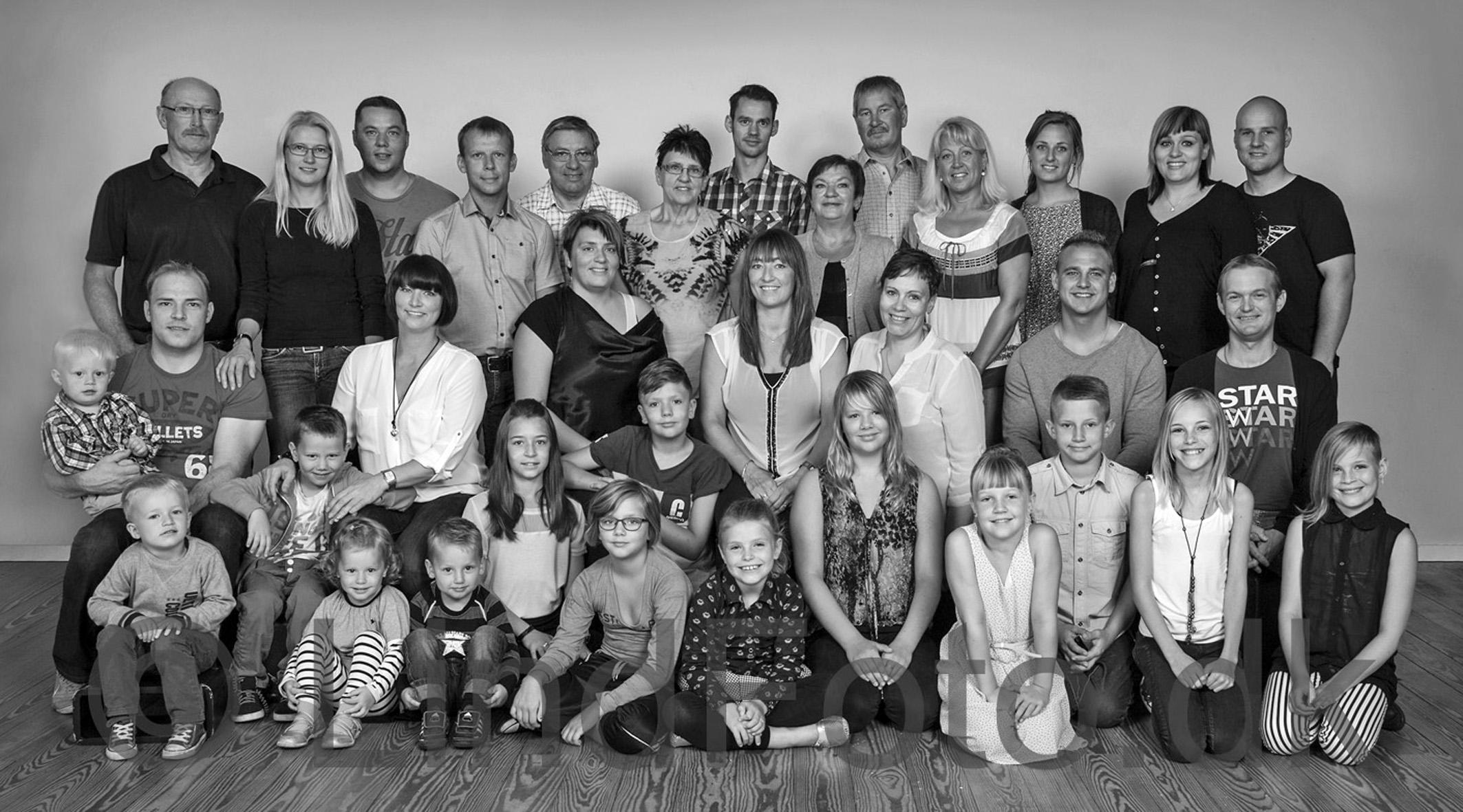 En stor familiegruppe med voksne og børn, der står og sidder sammen i en lys baggrund.