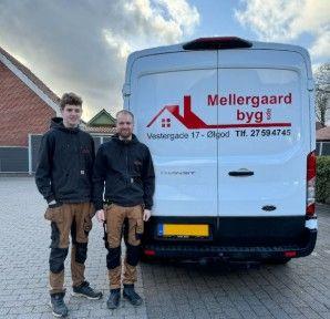 To personer i arbejdstøj står foran en hvid varevogn med teksten "Mellergaard byg" på bagsiden.