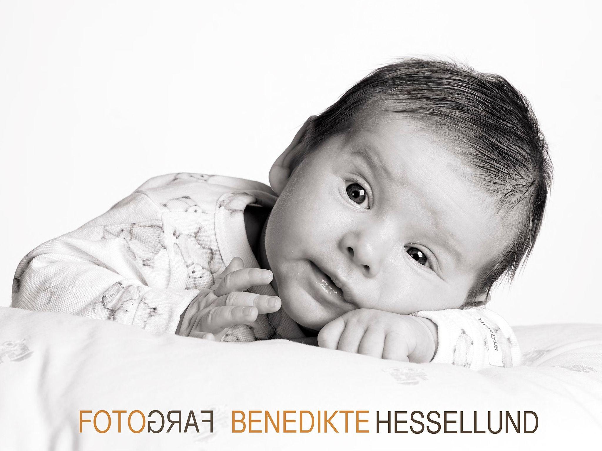 En sød baby ligger på maven med et nysgerrigt udtryk og ser op mod kameraet.