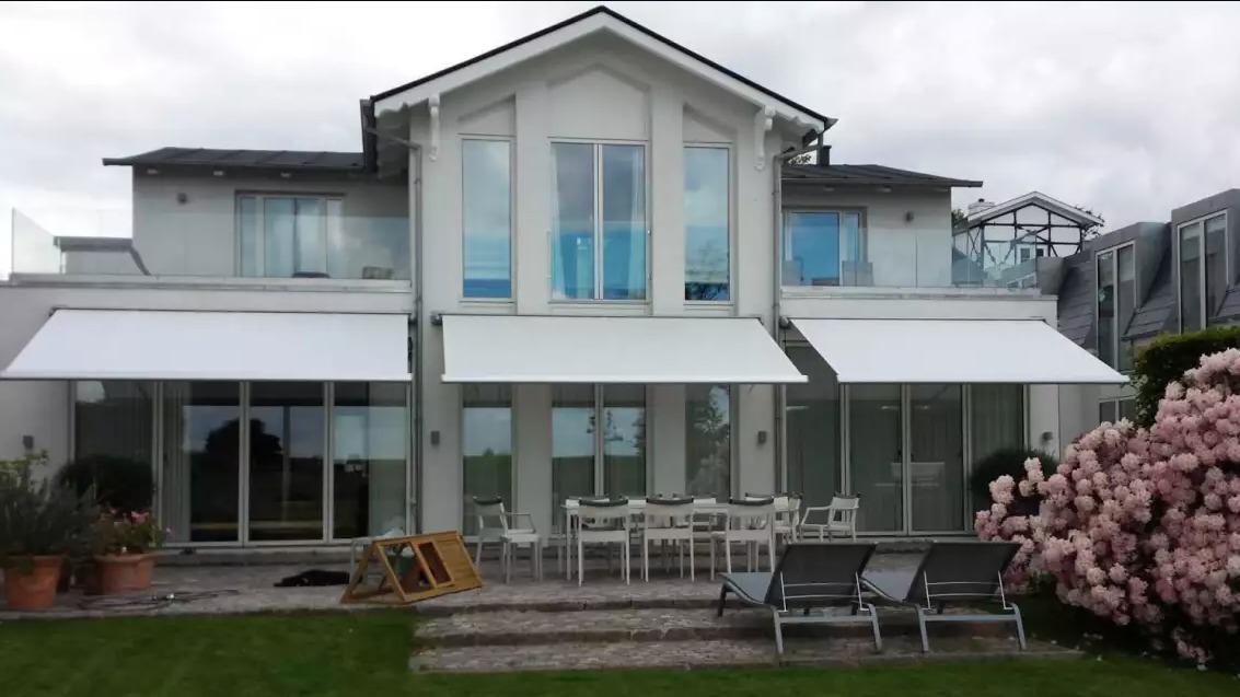 Moderne hus med store vinduer, markiser, terrasse og havemøbler i haven.