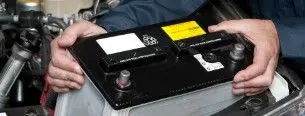 En person holder et bilbatteri, mens det installeres i motorrummet på en bil.