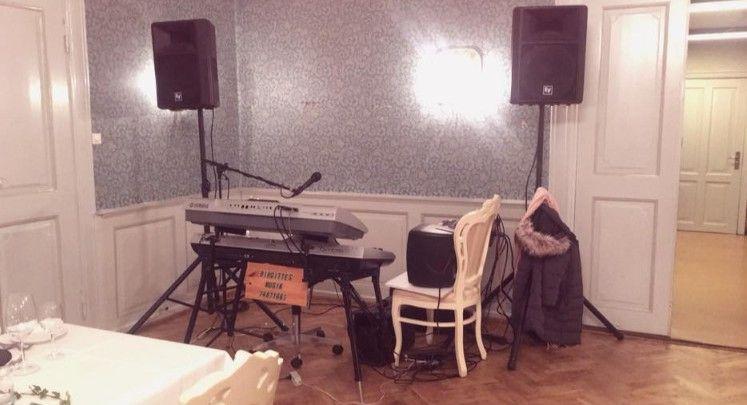 Et musiksetup med et keyboard, højttalere og en stol i et elegant lokale med vægdekoration.