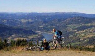 To personer på mountainbikes nyder udsigten over en dal med en sø og bjerge i baggrunden.