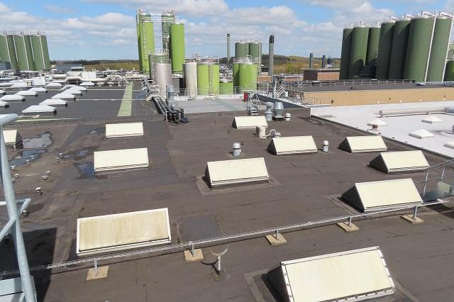 Oversigt over et industrielt tag med ventilationsskakter og grønne tanke i baggrunden.
