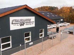 En moderne trailerudlejningsbygning med flere trailere parkeret udenfor og en person ved indgangen.