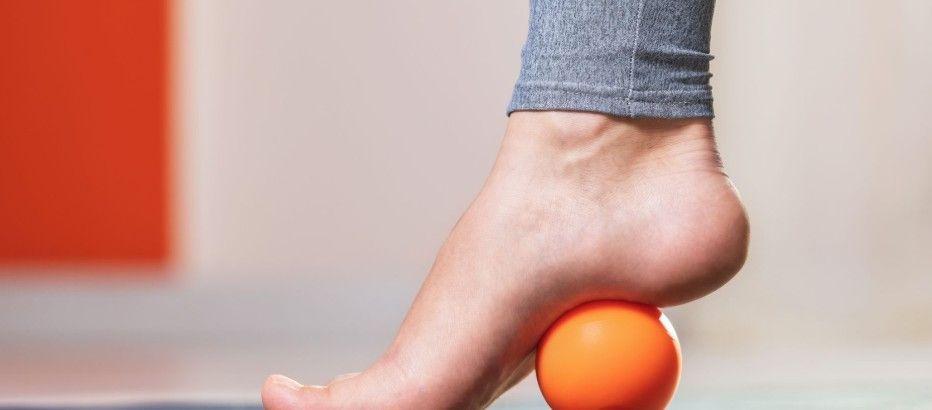En fod står på en orange bold, der bruges til fodmassage, med fokus på afslapning og velvære.